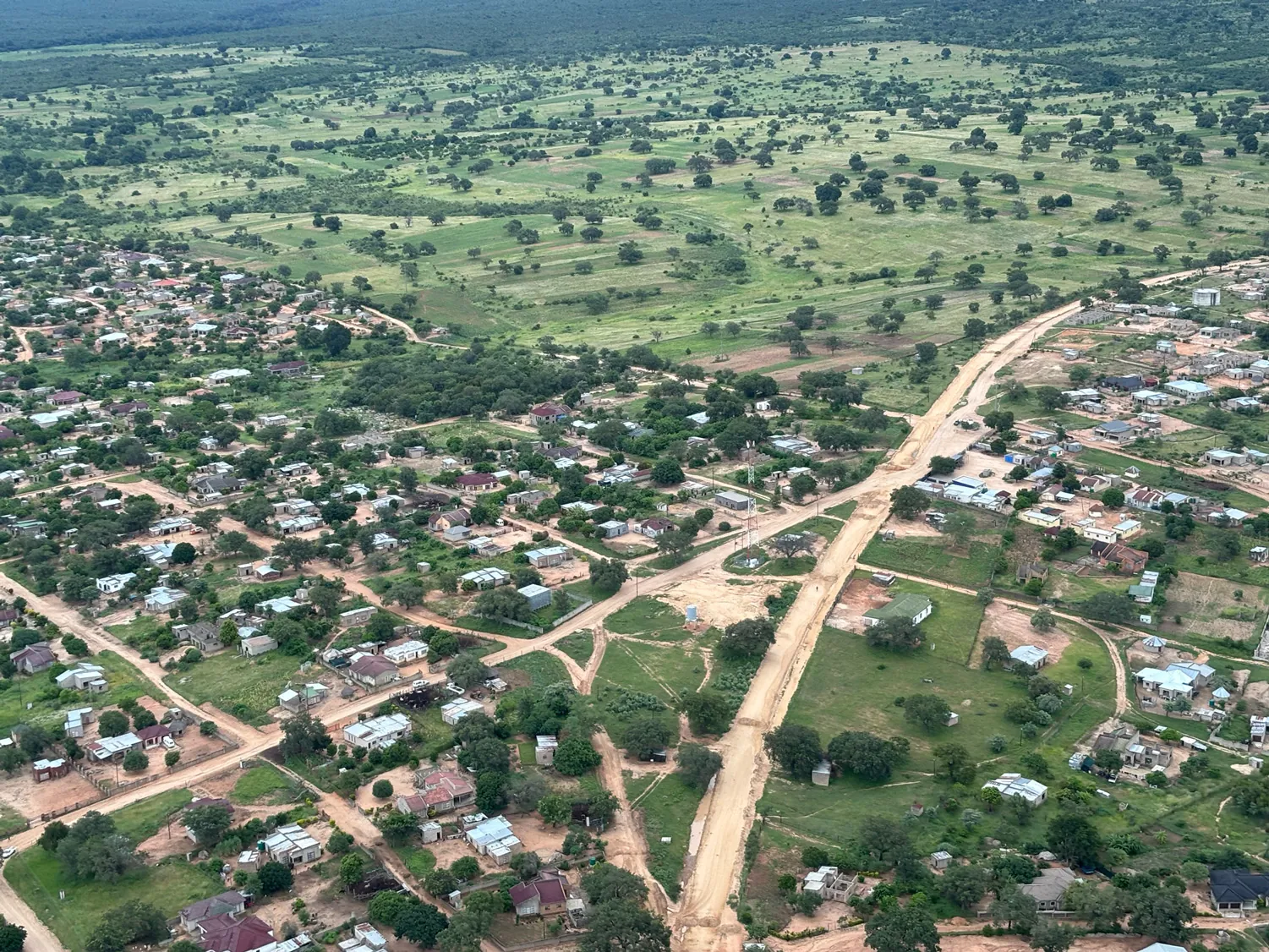 Aerial view of a village meeting the savanna bushland — the catchment landscape the carbon protects