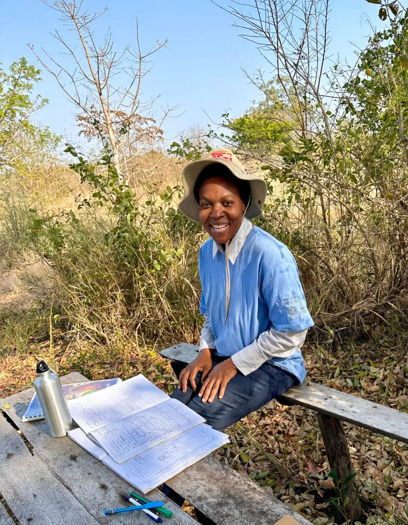 Nkhensani Dlamini at her farm outside Kruger Gate Road, seated at a bench with permaculture design sheets.