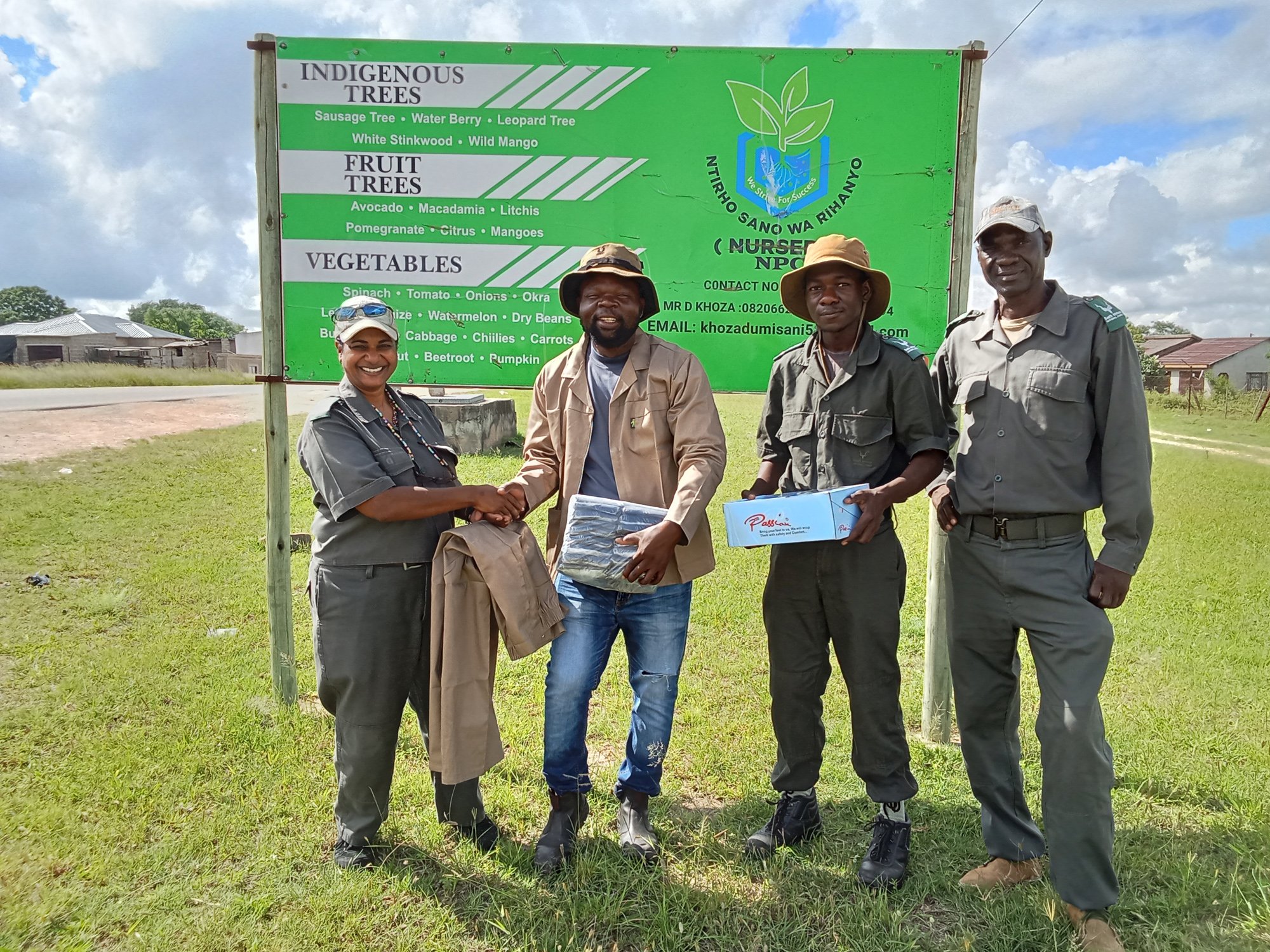 Project team and Ntirhisano Nursery operators stand together in front of the Ntirhisano Wa Rihanyi signboard at Lillydale during a handover of PPE and planting bags.